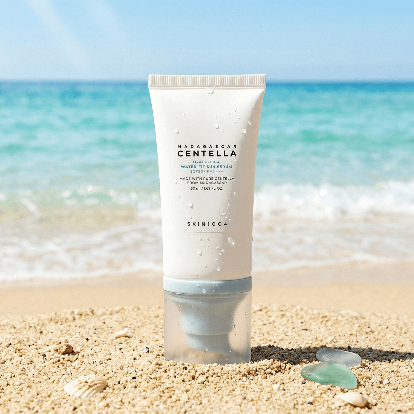 SKIN1004 SPF50 veido serumas paplūdimyje ant smėlio su jūros fonu
